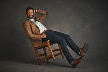 Portrait, chair and man with smile, studio and happy professor in mockup, relax and confident with style. Gray background, model and person on furniture, fashion and proud with jacket and rest