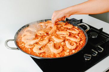 man adding some shrimps to a spanish fideua