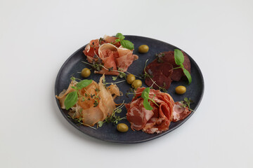Salami, sliced ham, sausage, prosciutto. Meat antipasti platter on ceramic black plate on the table
