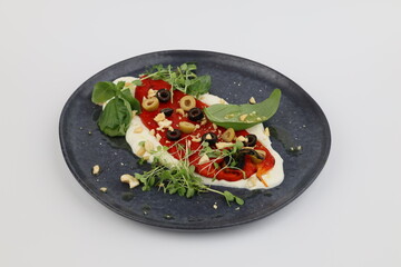 Baked peppers with feta cheese, olives and herbs on a beautiful dark plate on a white background