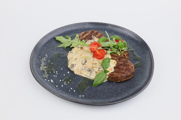 Veal medallions with mushroom sauce and greens on a dark plate on a white background