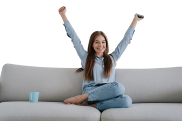 young woman sitting on a sofa, raising her arms in excitement while holding a remote control against transparent background, dressed in casual denim and a blue shirt. Concept of relaxation