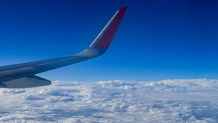 Fototapeta premium View from the airplane window at a beautiful cloudy sky and the airplane wing. Earth and sky as seen through window of an airplane