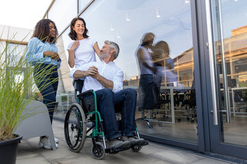 Two women talking to a man on a wheelchair near the office building