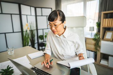 Mature japanese woman with earphones work at office on laptop