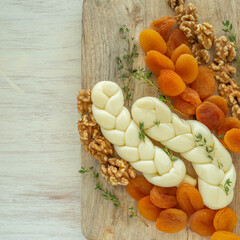 Cheese board for Jewish holiday Shavuot, for Harvest. Braided mozzarella cheese, walnuts, dried apricots, fresh thyme on wooden background.