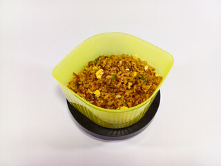 Nasi Goreng, Indonesian fried rice with meat, eggs, and vegetables, served in a yellow-green transparent container against a white background, showcasing a vibrant and flavorful dish