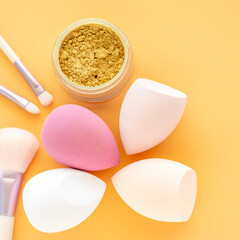 Cosmetic sponge and brush for powder on orange background.