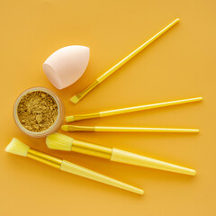 Sponge and brush for powder and cosmetic on yellow background.
