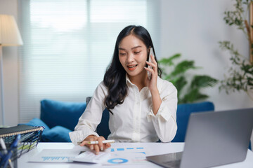 Fototapeta premium Young businesswoman is working from home, talking on the phone and analyzing financial charts