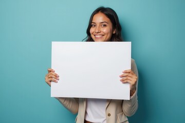 Fototapeta premium Smiling Woman Holding a Blank White Sign in Front of a Blue Background