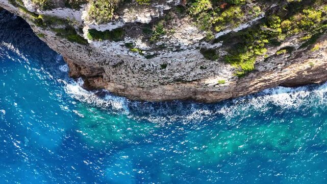Veduta aera della roccia a picco sul mare.
Il mare verde e cristallino si infrange sugli scogli della cosa Blanca in spagna