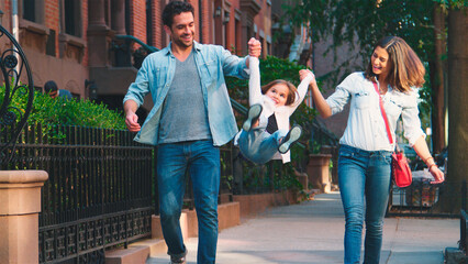 Family Shot With Parents Swinging Daughter As They Walk Along Urban Street In New York City 