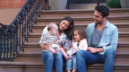 Family With Young Children Sitting Steps Outside Home On Urban Street In New York City USA