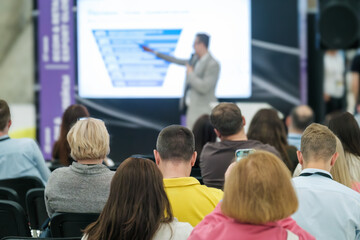 Speaker presenting information to an attentive audience at a business conference, focused on...
