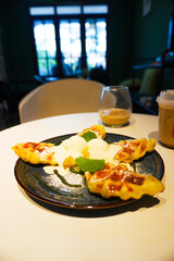 Close-up of waffles with ice cream and a drizzle of sauce on a blue plate, with a cup of coffee and a glass of iced tea in the background.