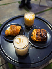 Two iced coffees, a croissant, and a chocolate pastry on a black round table.