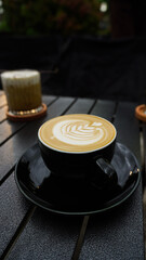 A cup of latte with a leaf design in the foam, on a table with a blurred background.