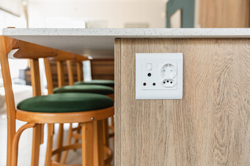 Plug point mounted on the side of a kitchen island, wood look cabinets, white stone surface, green...