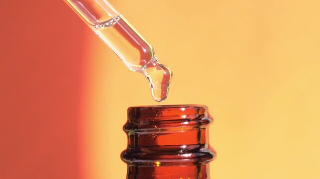 macro glass pipette with liquid fluid oil or serum drops on orange background with sunlight and shadow, cosmetic liquid skin care product