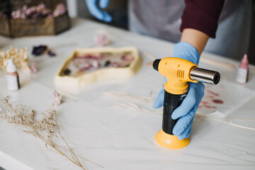 Artist using heat gun to craft resin art with dried flowers, merging creativity with scientific...