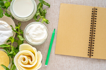 Blank notebook paper, dour cream, milk, mozzarella cheese, camembert, fresh mint on cotton fabric background.