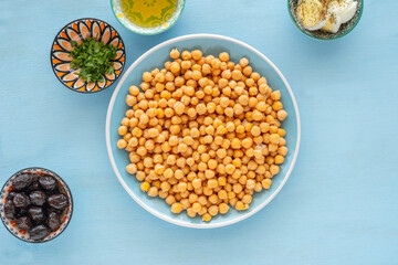 Plate of chickpeas served with black olives, chopped parsley on blue wooden background.