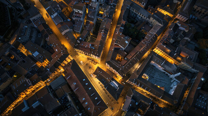 Obraz premium Aerial view of a historic city center at night, with ancient buildings softly lit by streetlights, narrow alleyways winding through the city, and the old blending with the new