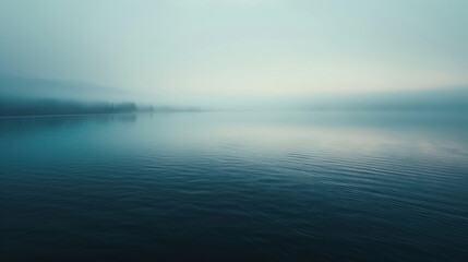 Obraz premium Aerial view of a fog-covered lake at dawn, with the still water reflecting the muted light of the sky, the shoreline blurred by the mist