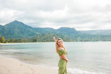 A stylish blonde in a green suit poses on the beach against the background of the mountains, Kauai, Hawaii