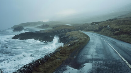 Fototapeta premium A solitary road along a rocky coastline, with waves crashing against the shore, the landscape bathed in the soft light of dawn, and mist rising from the sea