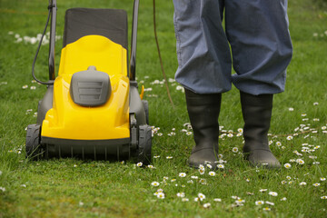 Fototapeta premium Gardener in black rubber boots trimming lawn with mower 