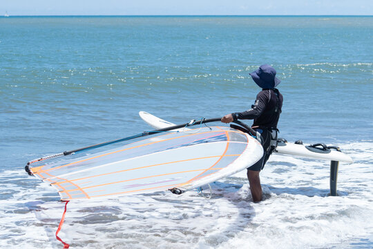 A male surfer prepares for windsurfing on the beach