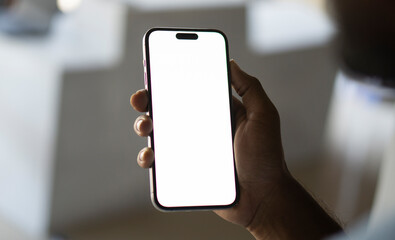Young man Holding Smartphone with Blank White Screen in Modern Indoor Setting, Perfect for Mockups and Digital Content.