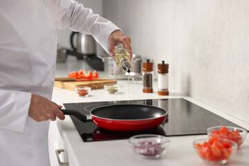 Professional chef pouring oil into frying pan in kitchen, closeup
