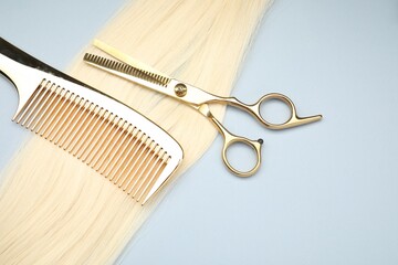 Blonde hair strand, comb and professional scissors on light grey background, top view