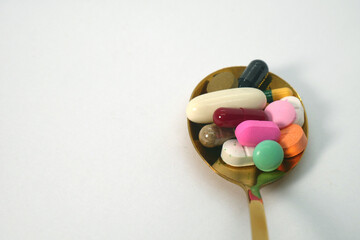 close up of colorful medicine tablets, capsules, and pills in the golden spoon on the white background isolated