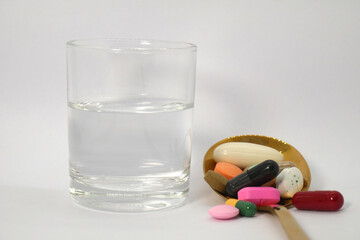 close up of colorful medicine tablets, capsules, and pills in the golden spoon with the glass of water beside on the white background isolated