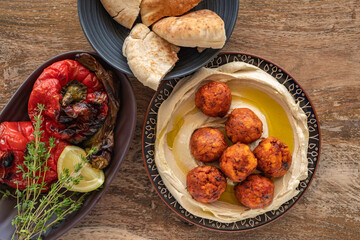 Hummus plate with meat balls, baked peppers, fresh thyme, pita bread for Mediterranean lunch over wooden background. Top view.