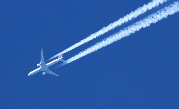 Jet airplane flying overhead in clear blue sky diagonally with condensation trail	