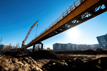Obraz premium A construction site featuring a yellow crane and an under-construction bridge against a clear blue sky.
