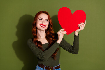 Photo of shiny attractive lady dressed shirt rising big red heart looking empty space isolated green color background