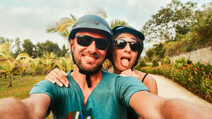 Portrait crazy authentic young happy caucasian couple take smartphone selfie while having fun driving scooter on tropical road trip in southeast asia. Couple in love having fun travel in asia © Evaldas