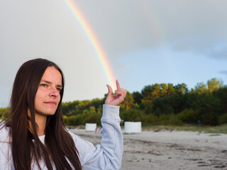 A Woman Young Brunette stands by the shore, her hand delicately grasping a Rainbow. The Rainbow's...