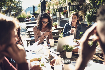 People, students and happy at restaurant for group assignment on teamwork and collaboration. Coffee shop, friends and university classmates with technology for research or revision for project