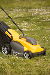 Yellow lawn mower on the spring green grass in the yard