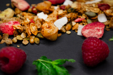 Honey, crispy, golden handmade granola with nuts, coconut, banana, seeds, bright strawberries and raspberries. A sprig and leaves of mint add freshness. Gray background, copy space, text place, banner