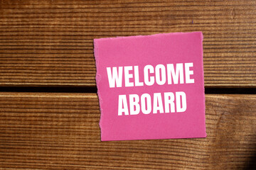Welcome aboard message written on ripped torn pink paper with wooden background. Conceptual welcome...