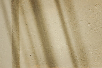 A wall with a shadow on it. The shadow is long and thin. The wall is made of concrete