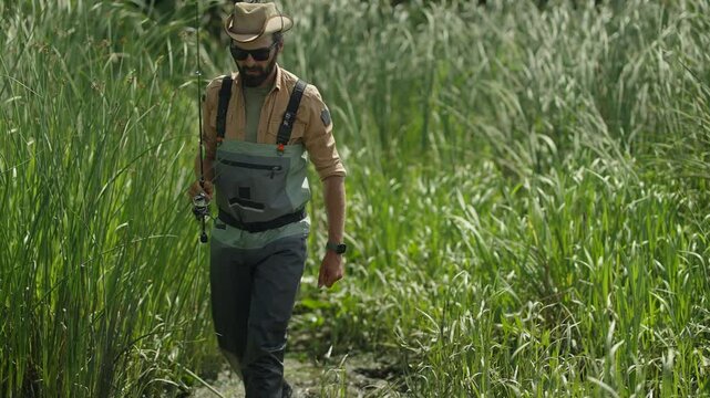 Man with spinning rod wades through reeds sinking into the mud